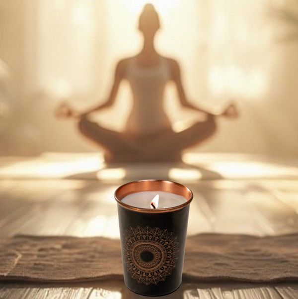 Candle with decorative design casting a shadow of a person in a meditative pose on a wooden floor.