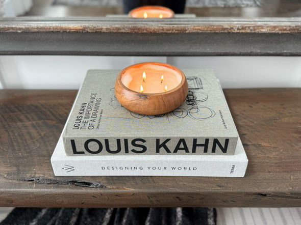 Wooden bowl candle on a book titled 'Louis Kahn' on a wooden surface.
